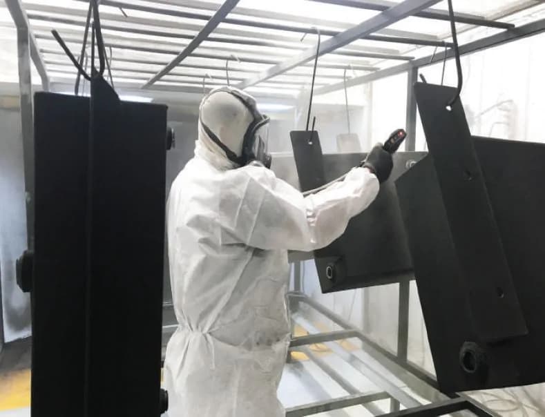Worker powder-coating steel parts in the Ledwell paint booth