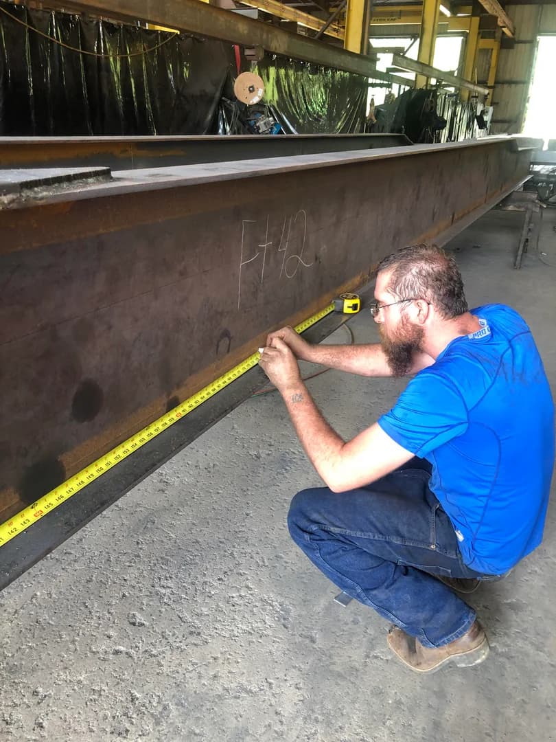 Worker measuring a steel main beam before fabrication