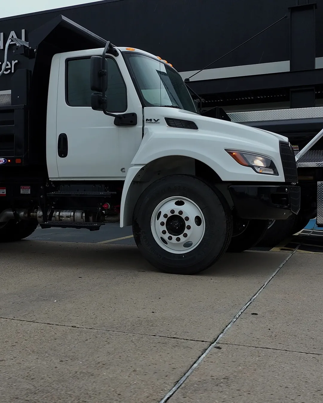 White tandem-axle International HV dump truck with a black Ledwell steel dump body, front three-quarter view on a dealer lot